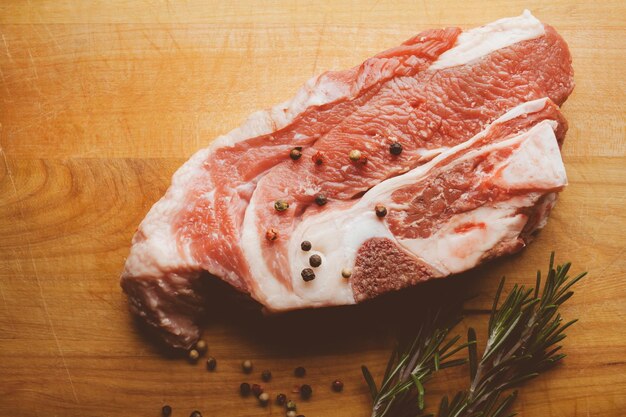 Schweinesteak mit Rosmarin und Pfeffer auf Holzhintergrund Rohes Fleischsteak Vintage-Fotoverarbeitung