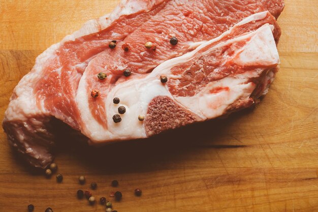 Schweinesteak mit Rosmarin und Pfeffer auf Holzhintergrund Rohes Fleischsteak Vintage-Fotoverarbeitung