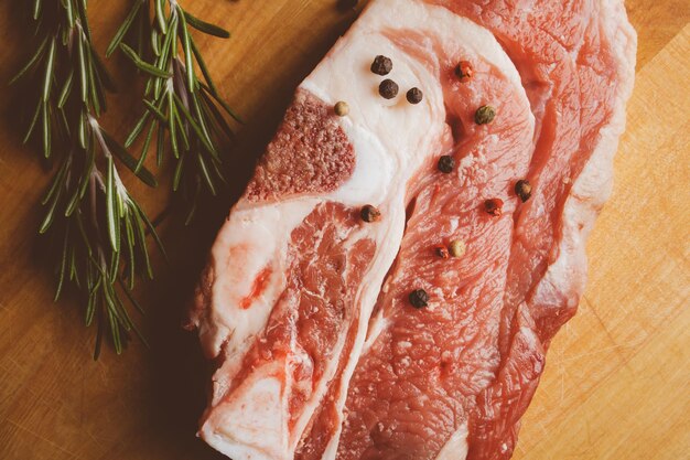 Schweinesteak mit Rosmarin und Pfeffer auf Holzhintergrund Rohes Fleischsteak Vintage-Fotoverarbeitung