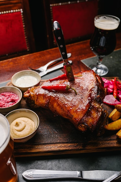 Schweinshaxe in Bier geschmort auf einem Holzbrett mit Senf-Meerrettich-Weißsauce Sauerkraut Bier und Kartoffel Im Wirtshaus servieren