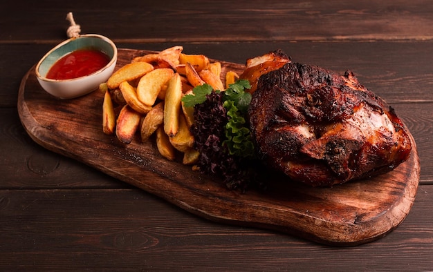 Schweinshaxe in Sojahonigsauce mit Bratkartoffeln auf einem Holzschneidebrett hausgemacht keine Leute