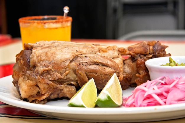 Schweinshaxe-Teller mit Zitronen, roten Zwiebeln, Guacamole und Getränk, Nahaufnahme, mexikanisches Essen