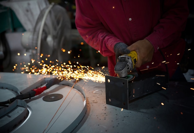 Schweißer benutzte Schleifstein auf Stahl in der Fabrik mit Funken, Schweißprozess in der Industriewerkstatt, Hände mit Instrument im Rahmen.