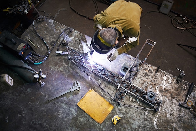 Schweißer schweißt Metalllayout eines Baukrans auf dem Eisentisch