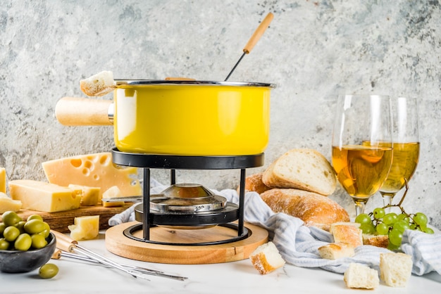 Schweizer Feinschmeckerfondue im traditionellen Fonduetopf mit Gabeln, verschiedenen Käsesorten, Oliven, Brot und Trauben