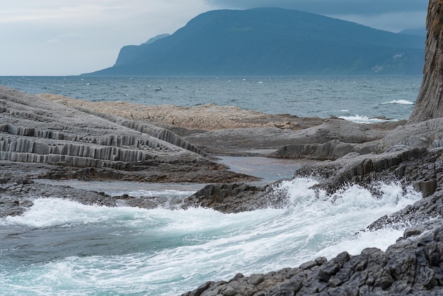 Schwere felsige Küste aus säulenförmigem Basalt vor dem Hintergrund einer stürmischen Meeresküstenlandschaft der Kurilen