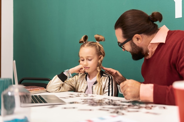 Schwere Frage. Hübsches blondes Mädchen mit Armbändern an ihrer Hand, die verwirrt betrachtet, während sie an die Buchstaben denken