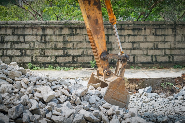 Schwerer organge Bagger mit der Schaufel, die auf Hügel mit Felsen steht