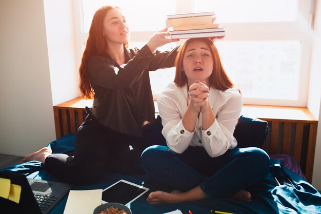 Schweres Lernkonzept. Ein Schüler legt dem anderen Bücher auf den Kopf. Zweites Gebet für Glück und Verständnis