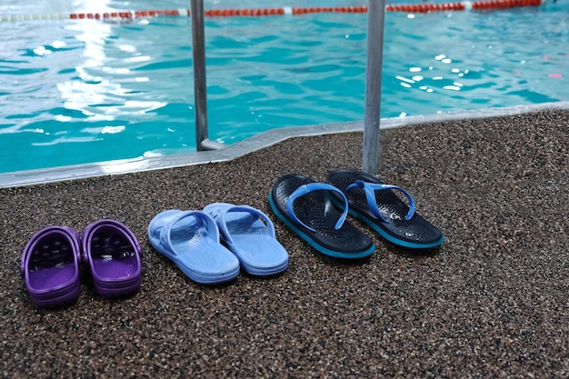 Foto schwimmbad. drei paar gummislipper stehen nebeneinander - herren-, damen- und kinderschuhe. familienabo für den pool.