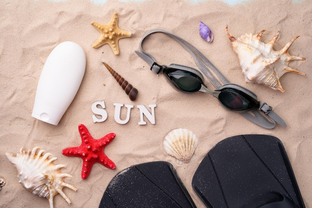 Schwimmbrillenflossen und Sonnencreme auf dem Sand mit Muscheln und Seesternen