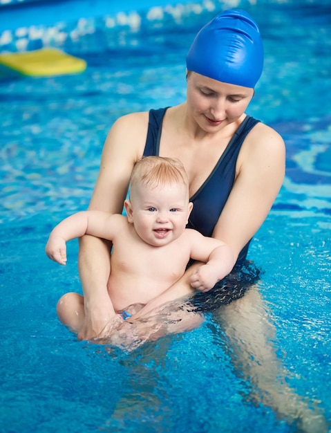 Schwimmen für Kleinkinder Porträt der jungen Mutter, die lachendes Kind in ihren Armen betrachtet Mutter, die mit Baby im Pool schwimmt