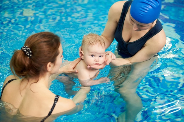 Schwimmerbaby, das in die Kamera schaut, während es bei Schwimmkursen im Planschbecken in Wasser eintaucht Schwimmtauchen unterrichten