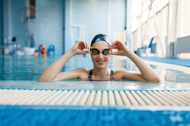 Schwimmerin im Badeanzug, Badekappe und Brille posiert im Pool