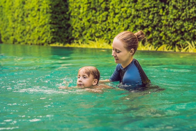 Schwimmlehrerin für Kinder bringt einem glücklichen Jungen das Schwimmen im Pool bei