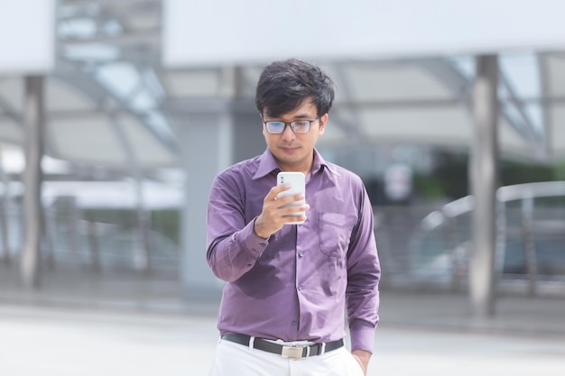 Schwitzender junger asiatischer Geschäftsmann, der sich Nachrichten auf dem Handy ansieht, während er auf der Straße geht.