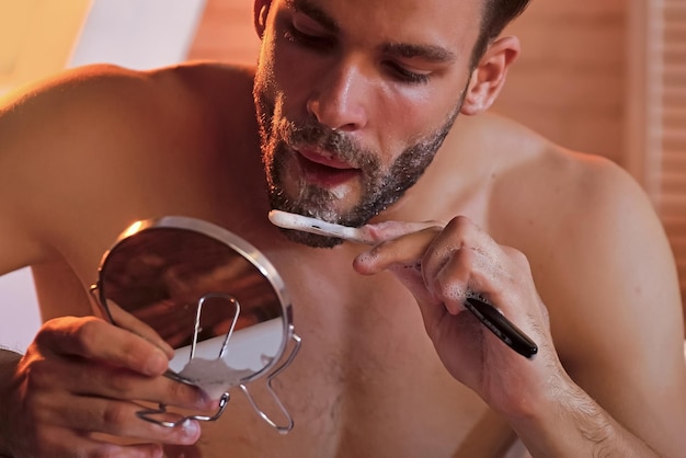 Schwul mit Rasierseife auf Barthaar im Spiegel Rasieren Friseur Friseursalon Hygiene Gesundheit Bärtiger Mann rasiert sich mit Rasiermesser Hautpflegebehandlungstherapie