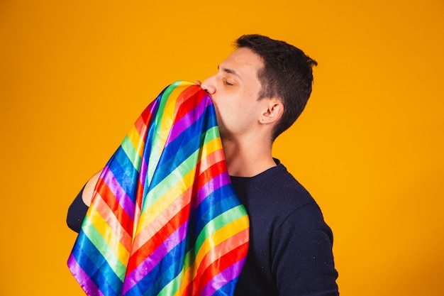 Schwulenstolz. Homosexueller Junge, der lgbt-Flagge auf gelbem Hintergrund küsst.