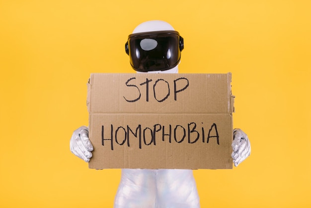 Schwuler Mann, der als Astronaut mit Helm und silbernem Anzug verkleidet ist und ein Schild mit der Aufschrift 39Stop Homophobia39 auf gelbem Hintergrund hält Homosexuelle homosexuelle Transrechte und Geschlechterstolzkonzept