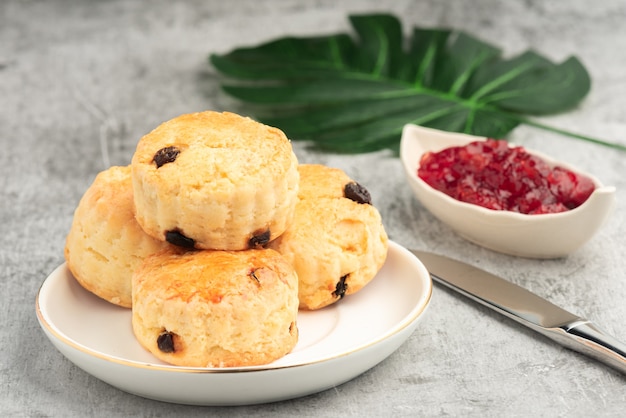 Scone en plato blanco y mermelada de fresa sobre fondo de cemen