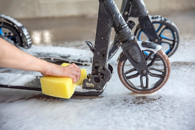 Scooter de limpeza. Cuidados com scooters elétricos. A mão de uma mulher lava uma scooter com uma esponja com espuma em um lava-rápido. Lugar para o seu texto.