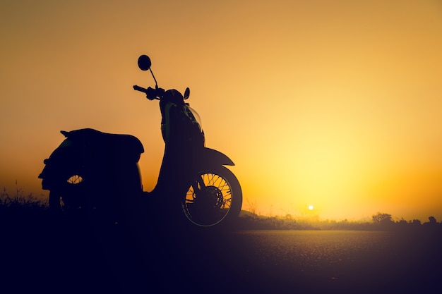 Scooter de silhueta em pé no campo ao pôr do sol