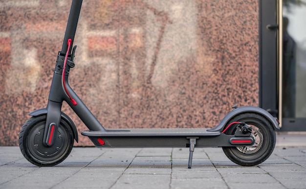 Scooter eléctrico estacionado en pavimento de baldosas - detalle de primer plano, pared de mármol y fondo de puerta de vidrio