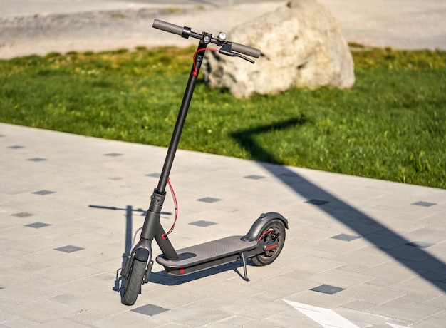 Scooter eléctrico estacionado en el pavimento de piedra de baldosas de fondo de césped verde