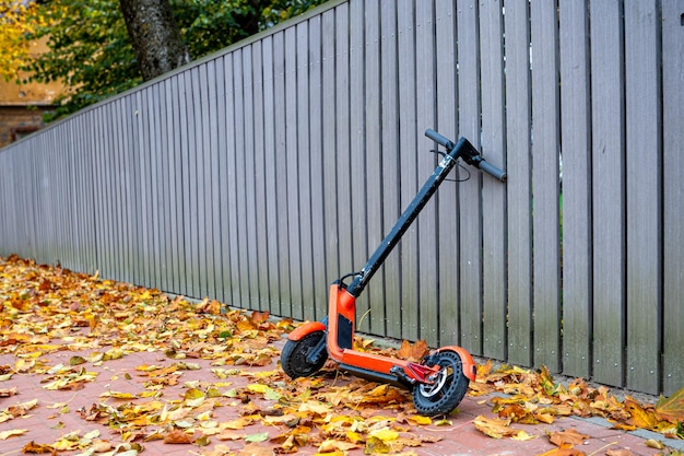 Scooter elétrica na beira de uma calçada coberta com folhas de outono por uma cerca de madeira