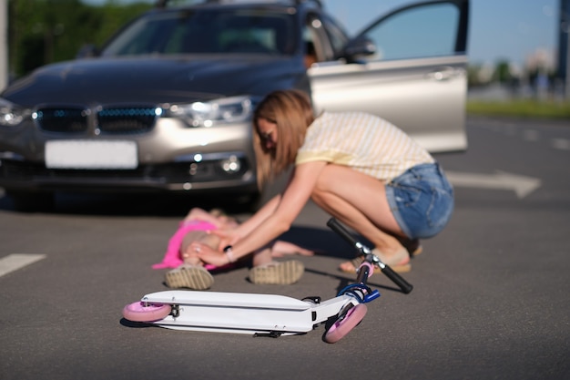 Foto scooter infantil deitada na frente de uma menina ferida em um acidente de carro.