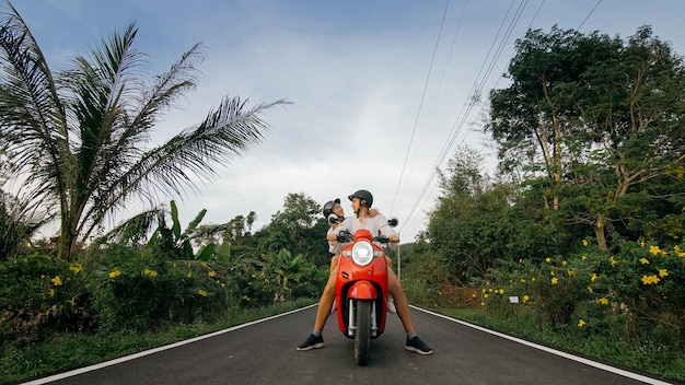 Scooter-Roadtrip Liebespaar auf rotem Motorrad in weißer Kleidung auf Forstweg