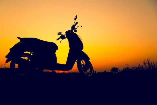 Scooter de silueta de pie en el campo al atardecer