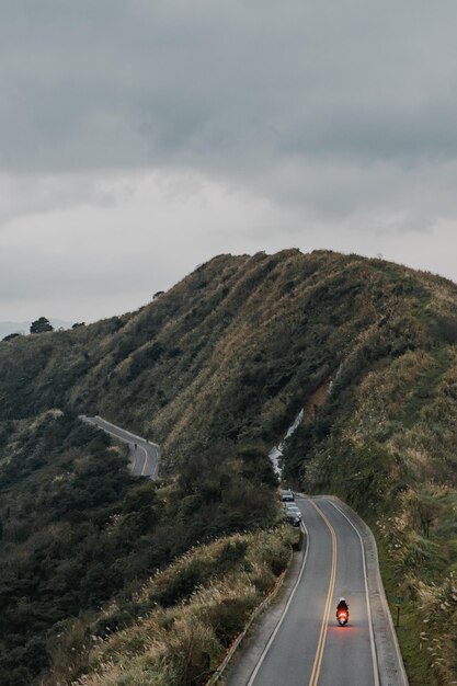 Foto scooter solitario montado en una carretera de campo por la montaña contra un cielo tormentoso