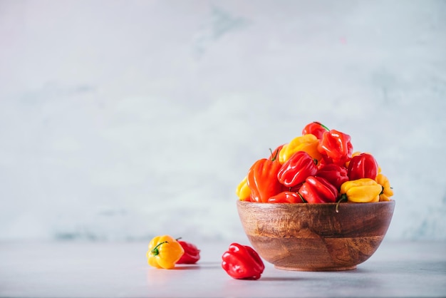 Scotch bonnet chiles amarillos y rojos en un tazón de madera sobre fondo gris Copiar espacio