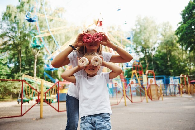 Se divertindo com donuts. Menina alegre, a mãe dela se divertir no parque juntos, perto de atrações.