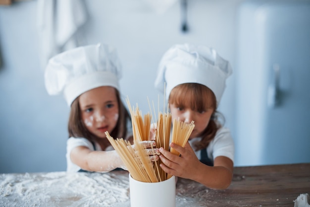 Se divertindo com espaguete. filhos da família com uniforme branco do chef, preparando a comida na cozinha.