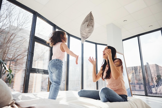 Se divertindo com travesseiro na cama Jovem mãe com sua filha passando fim de semana juntos no quarto