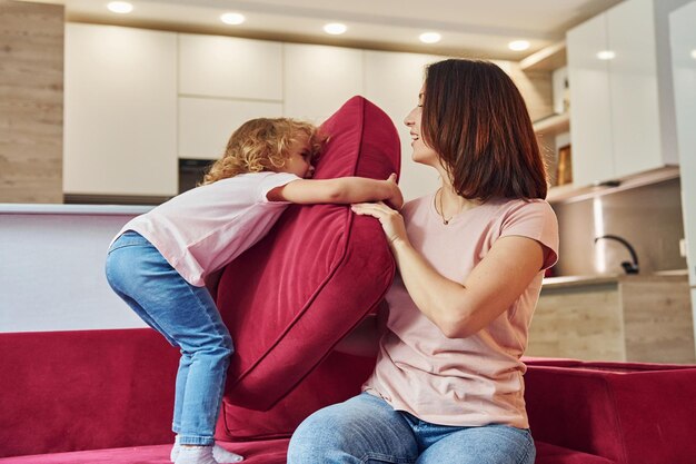 Se divertindo e pulando Jovem mãe com sua filha em roupas casuais juntos dentro de casa em casa