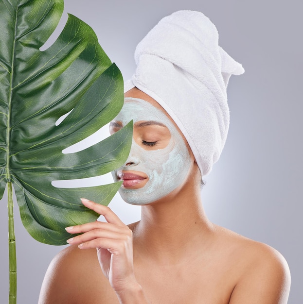 Sea amable con su piel. Foto de una joven atractiva con una máscara facial y sosteniendo una hoja de monstera en el estudio.