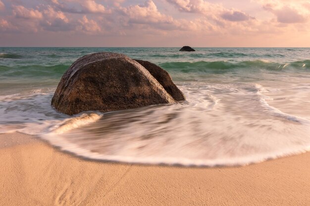 Seascape com rochas na água turquesa da praia arenosa e nuvens cor de rosa ao nascer do sol Samui Tailândia