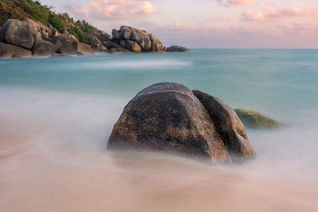 Seascape con rocas en la playa de arena agua turquesa y nubes rosas al amanecer Samui Tailandia