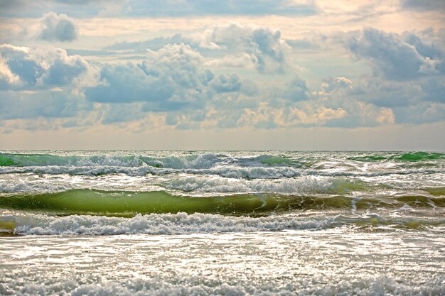 Seascape tempestuosa com céu nublado e mar acenando surf na areia marrom molhada Água do mar verde com ondas de espuma branca e silhueta escura da embarcação no horizonte do horizonte Cena de férias do mar