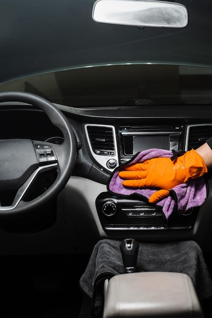 Foto secado manual del interior del automóvil con microfibra del salpicadero y multimedia en el detallado del servicio de automóviles trabajador de limpieza del interior del automóvil en seco etapa final del detallado de la limpieza en seco