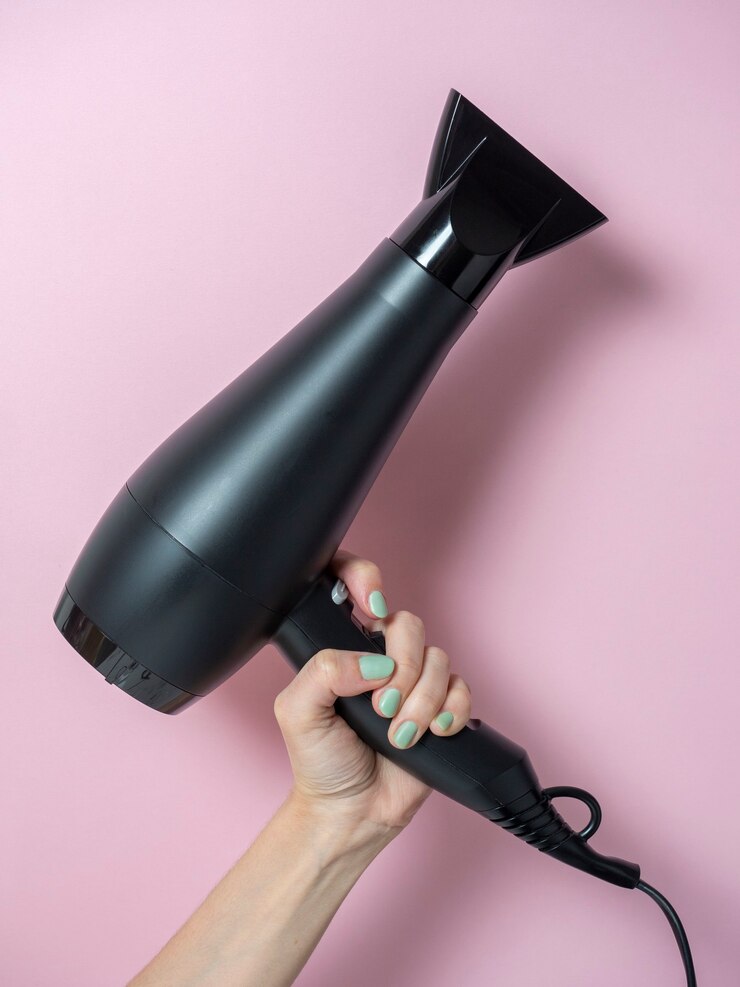 Secador de cabelo preto na mão de uma mulher em um fundo rosa. Produto para o cuidado do cabelo. Foto vertical