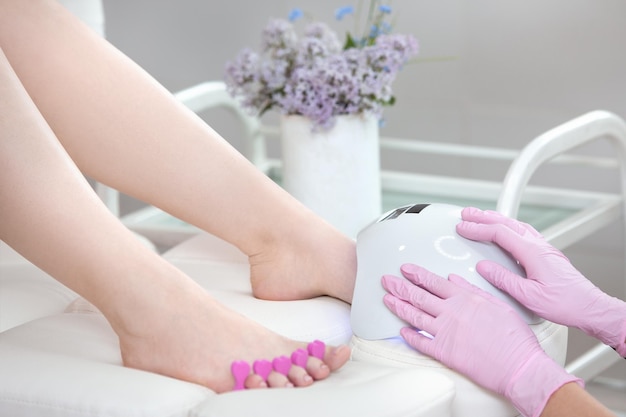 Secador de unhas secando as unhas dos pés com radiação ultravioleta No fundo de um buquê de lilás