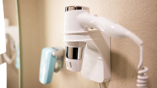 Secador de pelo eléctrico de plástico blanco en soporte de pared en el baño.