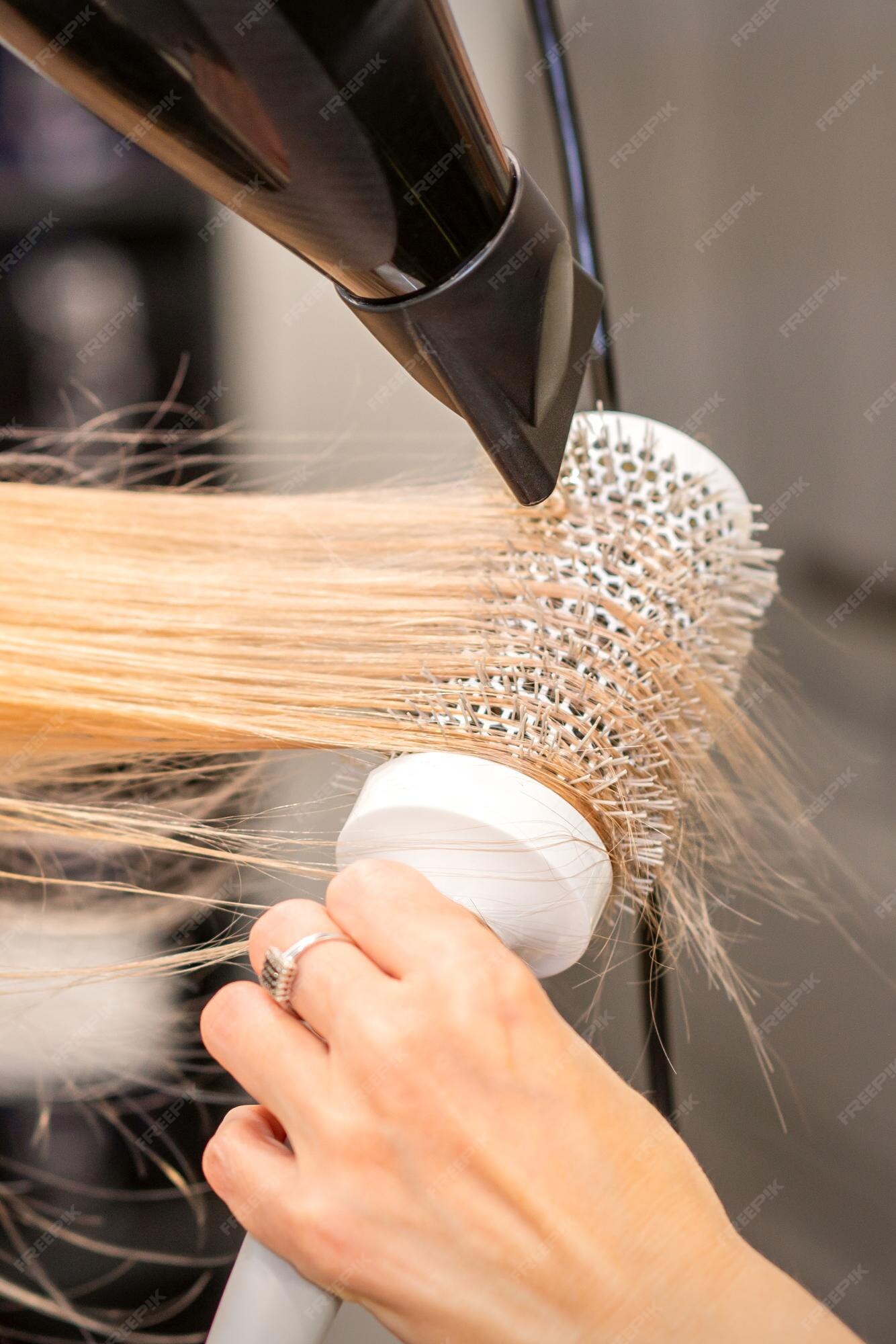 Secagem de cabelo no estúdio de cabeleireiro. estilista de cabeleireira  seca o cabelo com secador de cabelo e escova redonda ruiva de uma mulher em  um salão de beleza.