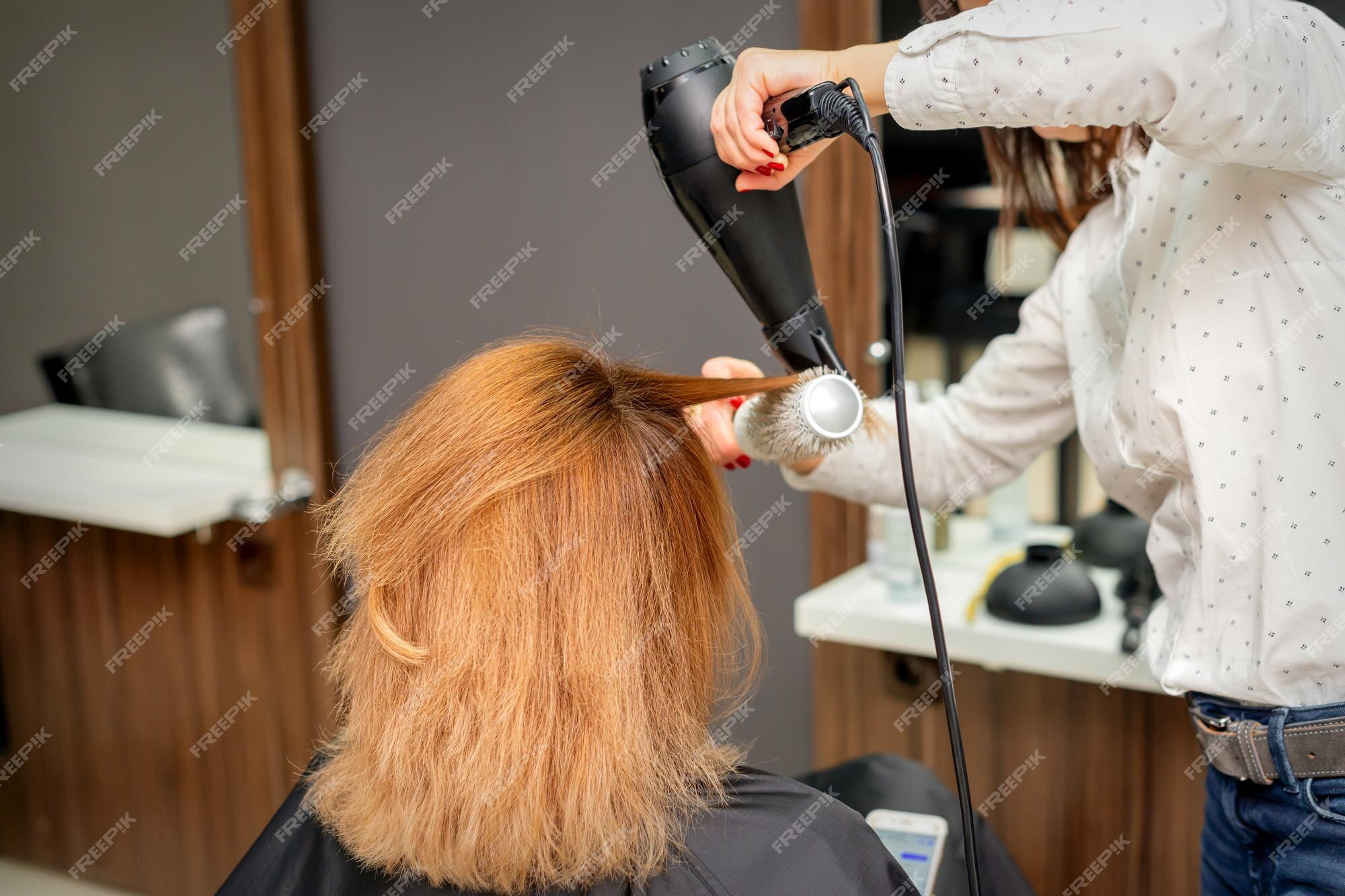 Cabeleireiro seca e modela o cabelo com um secador de cabelo no salão de  beleza