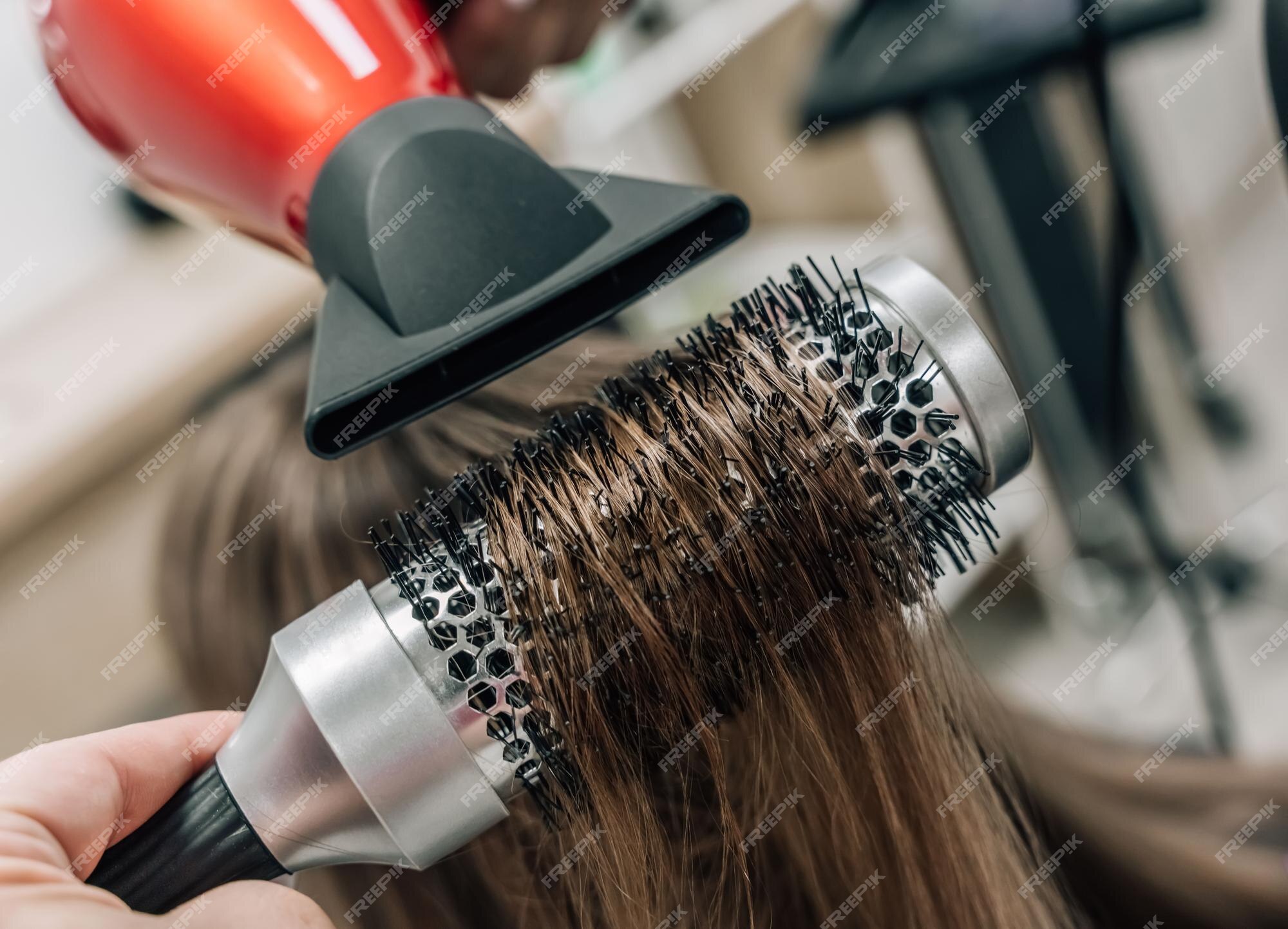 Secagem de cabelo no estúdio de cabeleireiro. estilista de cabeleireira  seca o cabelo com secador de cabelo e escova redonda ruiva de uma mulher em  um salão de beleza.