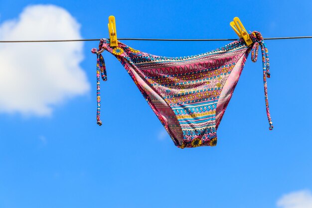 Foto secagem de maiô feminino pendurado em uma corda contra o céu azul conceito de férias de verão